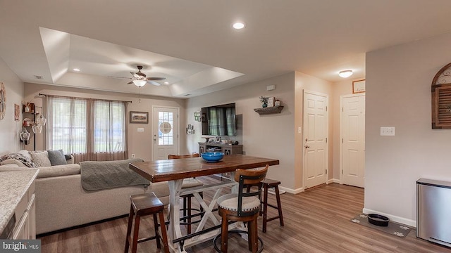 dining space with a tray ceiling, baseboards, a ceiling fan, and wood finished floors