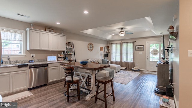 kitchen with a tray ceiling, stainless steel dishwasher, ceiling fan, a sink, and visible vents