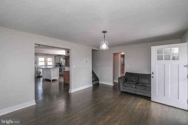 unfurnished living room with stairway, dark wood-style floors, and baseboards