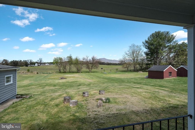 view of green lawn with an outdoor structure, a mountain view, a view of rural / pastoral area, and a storage unit