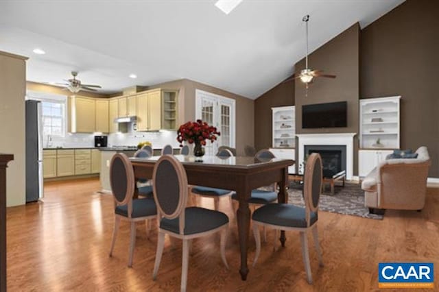 dining space with a fireplace, ceiling fan, lofted ceiling, and light wood-style floors
