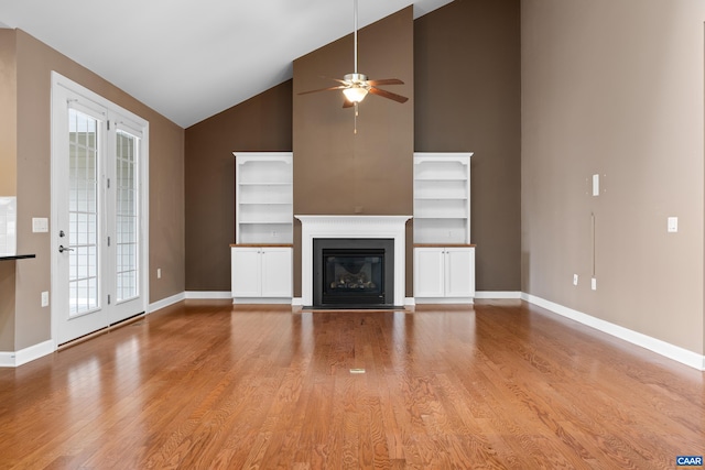 unfurnished living room with wood finished floors, a ceiling fan, high vaulted ceiling, plenty of natural light, and baseboards