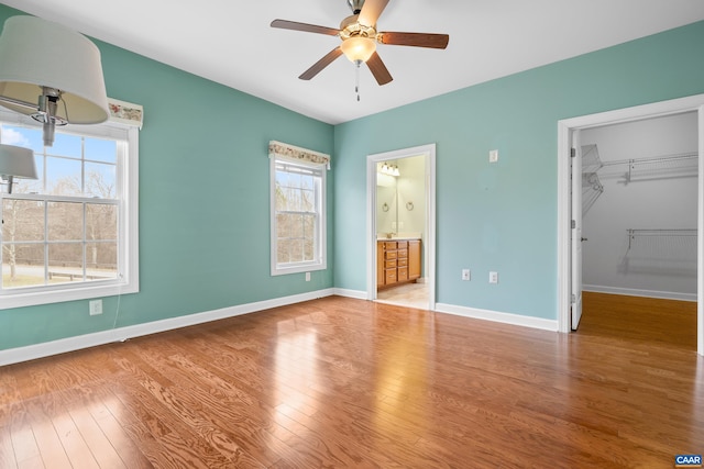 unfurnished bedroom with a closet, wood finished floors, a ceiling fan, a walk in closet, and baseboards