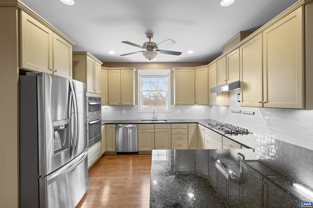 kitchen featuring a sink, stainless steel appliances, cream cabinetry, ceiling fan, and decorative backsplash