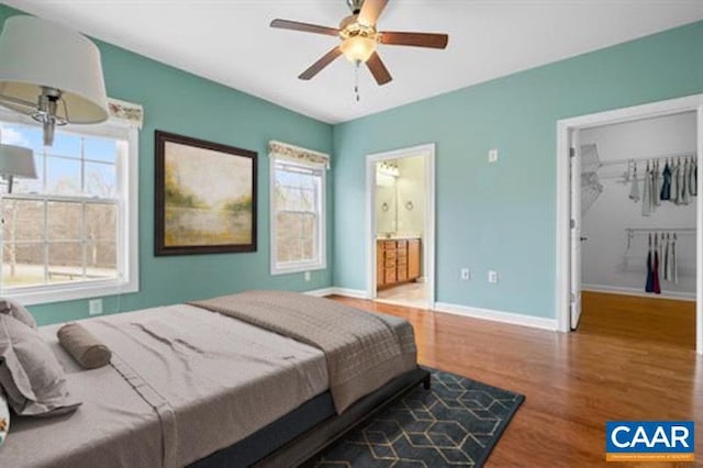 bedroom with baseboards, ceiling fan, connected bathroom, a walk in closet, and wood finished floors