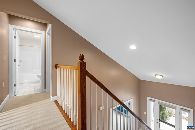 hall with vaulted ceiling, carpet flooring, baseboards, and an upstairs landing