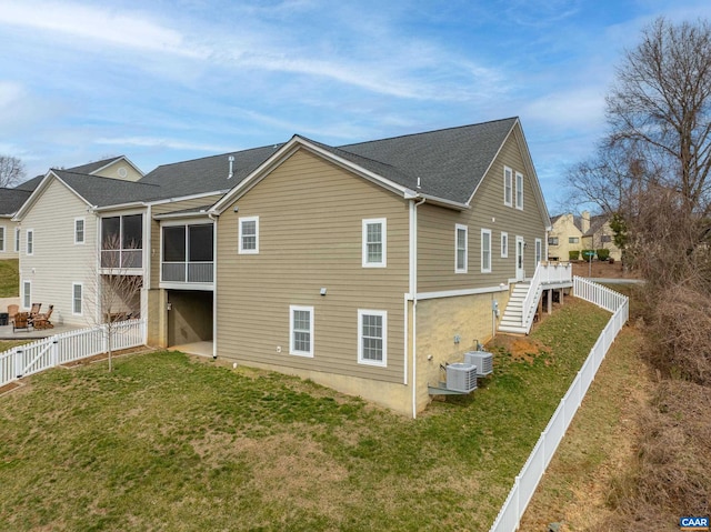 rear view of property featuring a lawn, stairway, a sunroom, and a fenced backyard