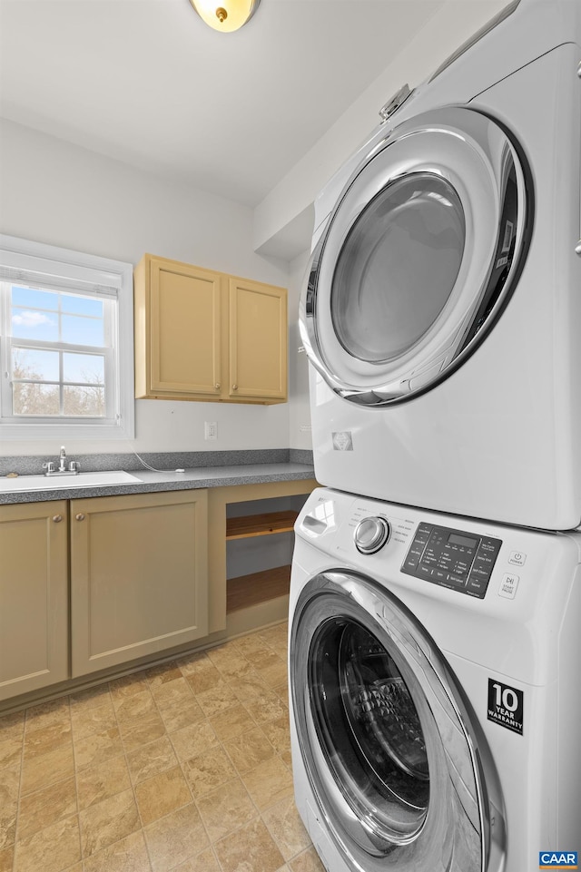 laundry area featuring stacked washer / dryer, cabinet space, a sink, and stone finish flooring