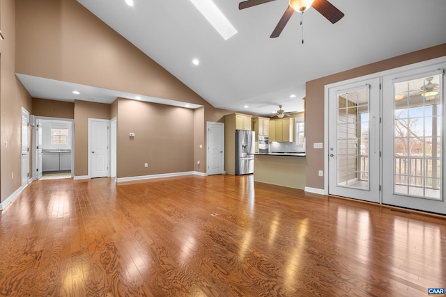 unfurnished living room with light wood-type flooring, baseboards, ceiling fan, and high vaulted ceiling