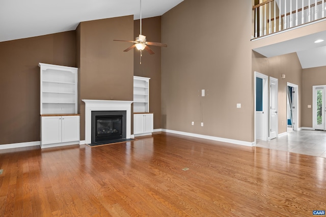unfurnished living room with a ceiling fan, baseboards, high vaulted ceiling, and wood finished floors