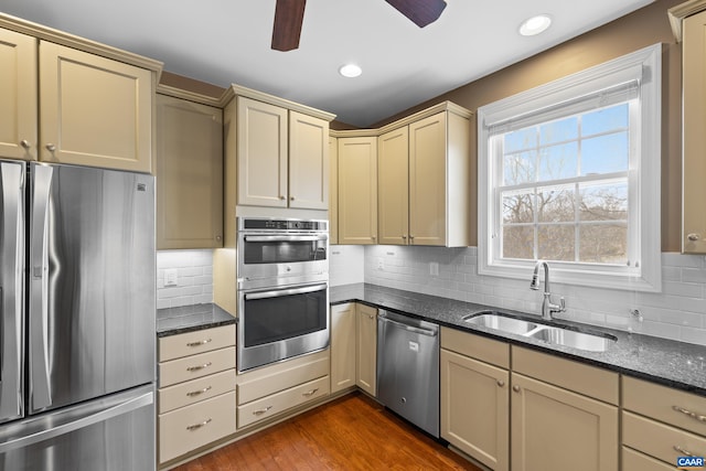 kitchen featuring ceiling fan, a sink, dark stone countertops, appliances with stainless steel finishes, and cream cabinets