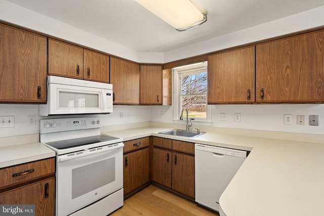 kitchen with white appliances, a sink, brown cabinets, and light countertops