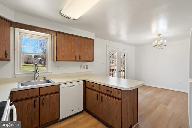 kitchen featuring white dishwasher, a sink, a peninsula, range, and light wood-type flooring