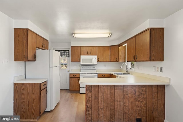 kitchen with white appliances, a sink, a peninsula, light wood-style flooring, and brown cabinetry
