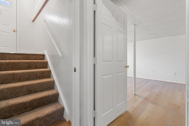 stairs featuring a drop ceiling, wood finished floors, and baseboards