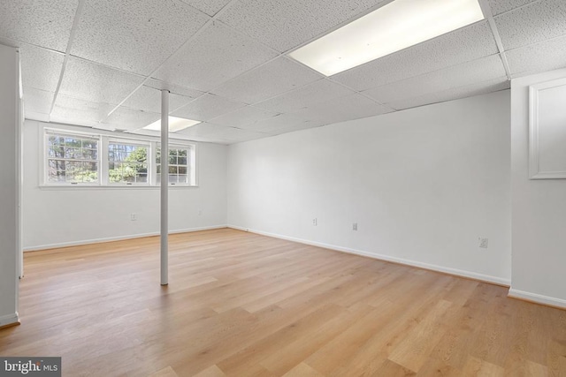 below grade area with a paneled ceiling, baseboards, and light wood-style floors
