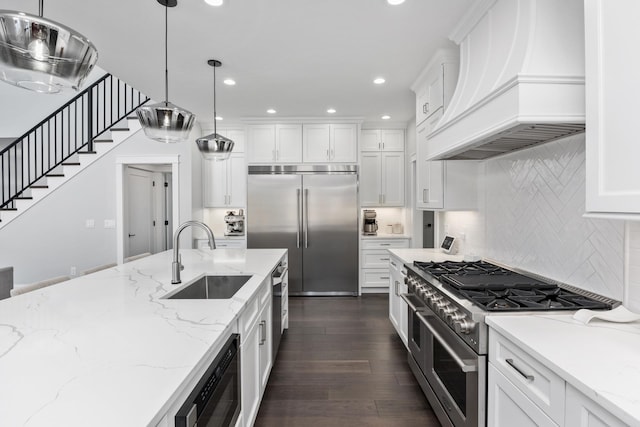 kitchen featuring hanging light fixtures, custom range hood, high quality appliances, and a sink