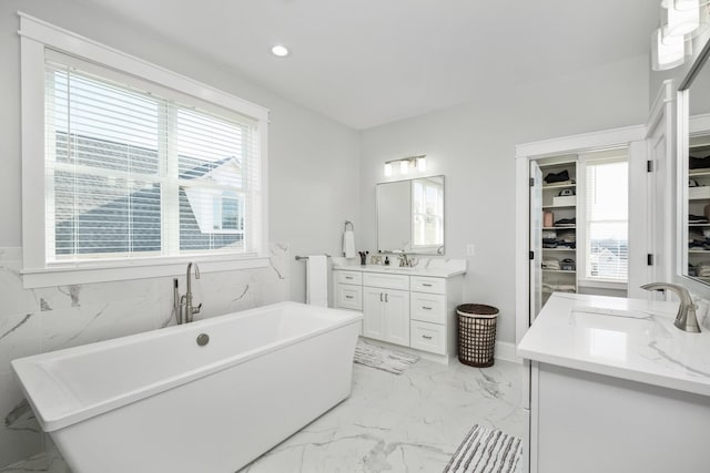 full bath featuring marble finish floor, recessed lighting, a spacious closet, vanity, and a freestanding tub