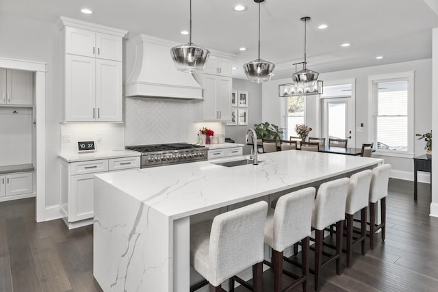 kitchen featuring premium range hood, a sink, white cabinetry, a large island, and decorative light fixtures