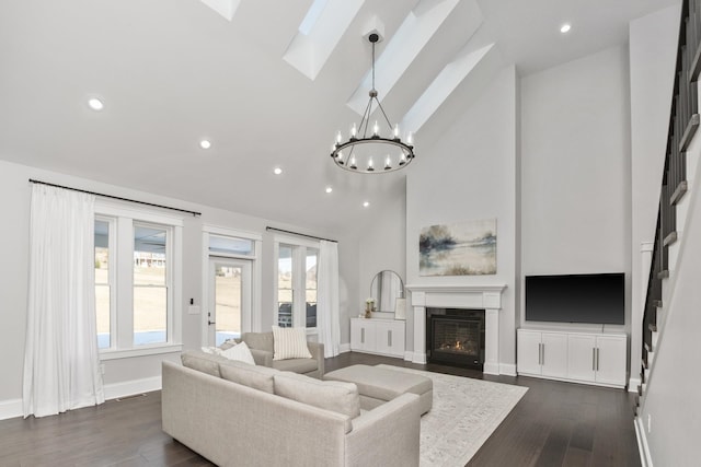 living room featuring a skylight, a chandelier, dark wood finished floors, and a glass covered fireplace