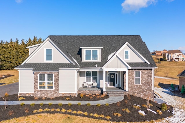 view of front of house with brick siding, a porch, a shingled roof, board and batten siding, and stone siding