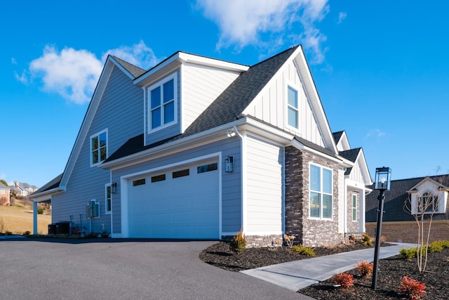 view of home's exterior featuring aphalt driveway, roof with shingles, an attached garage, board and batten siding, and stone siding