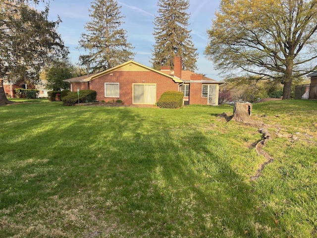 rear view of property with brick siding, a yard, and a chimney