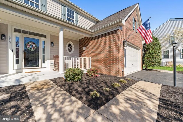 doorway to property with brick siding, covered porch, asphalt driveway, and an attached garage