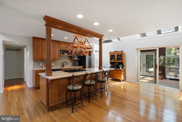 13013 Alum Springs Rd, Culpeper, VA 22701 - kitchen featuring brown cabinets, light countertops, light wood finished floors, backsplash, and a kitchen breakfast bar