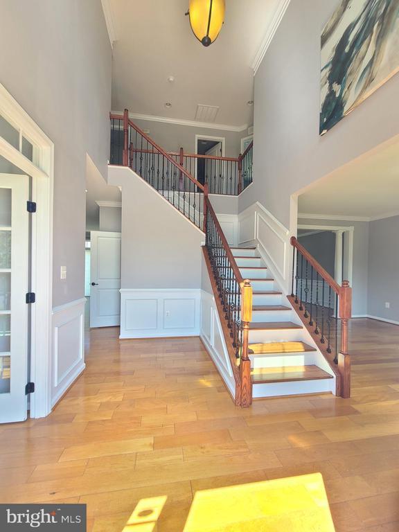9423 Reservoir Rd, Fredericksburg, VA 22407 - stairway with ornamental molding, a towering ceiling, wood finished floors, a decorative wall, and wainscoting