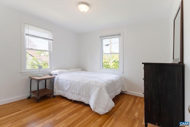 bedroom featuring multiple windows, light wood-style floors, and baseboards