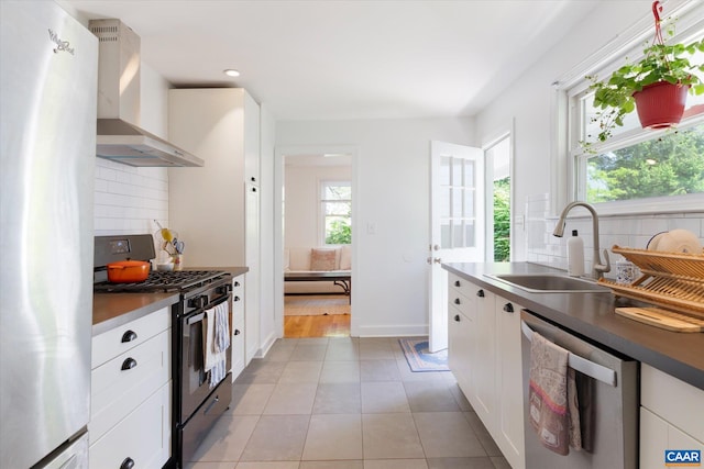 kitchen with stainless steel appliances, wall chimney exhaust hood, decorative backsplash, white cabinets, and a sink