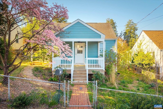 bungalow with a porch, a gate, roof with shingles, and a fenced front yard