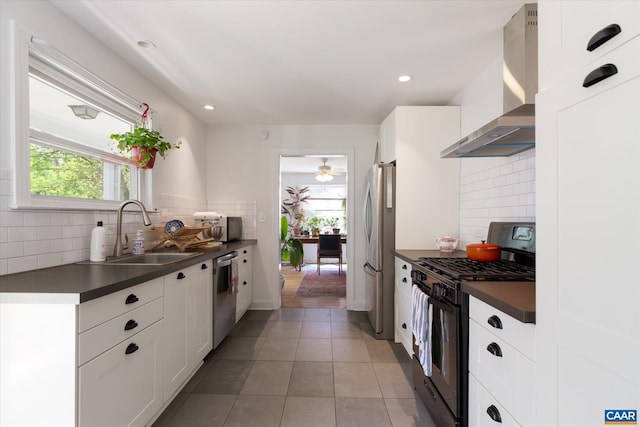 kitchen featuring appliances with stainless steel finishes, wall chimney range hood, dark countertops, a sink, and healthy amount of natural light