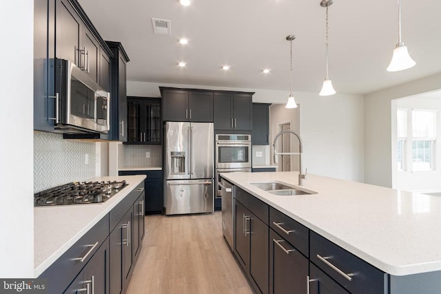 9003 Walnut Hill Rd, Fredericksburg, VA 22408 - kitchen featuring appliances with stainless steel finishes, backsplash, light wood-style flooring, pendant lighting, and a center island with sink