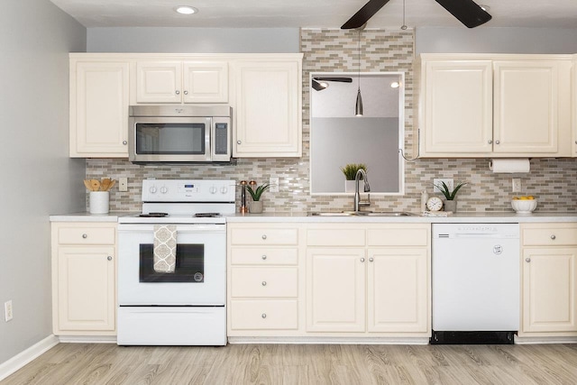 kitchen featuring white appliances, decorative backsplash, light countertops, light wood-style floors, and a sink