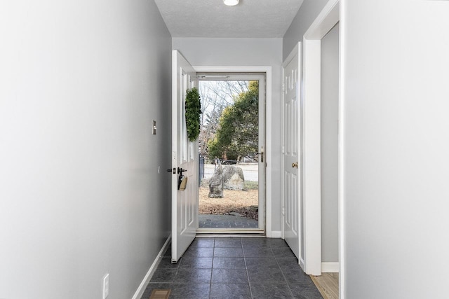 entryway with a textured ceiling, baseboards, and dark tile patterned floors