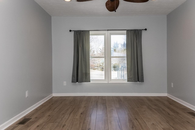 unfurnished room with a ceiling fan, visible vents, baseboards, and wood finished floors