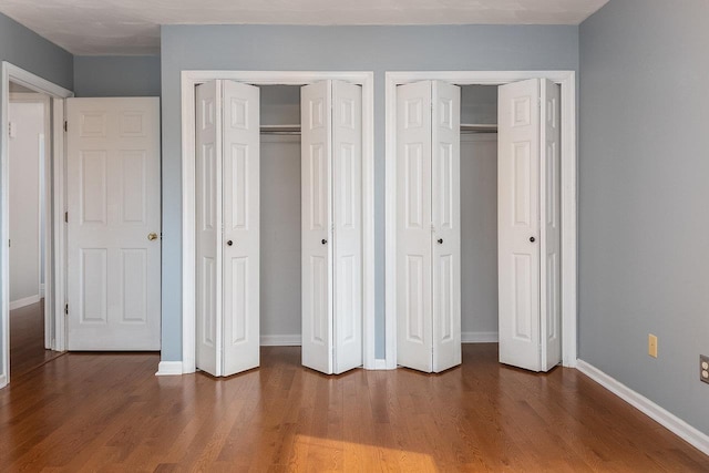 unfurnished bedroom featuring baseboards, wood finished floors, and multiple closets