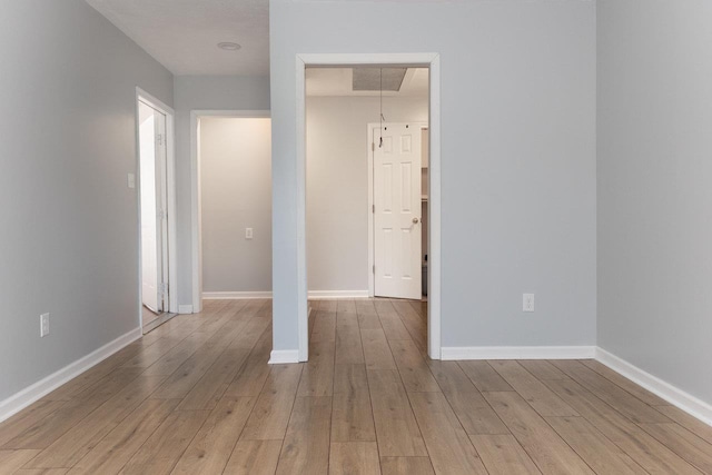 unfurnished bedroom featuring light wood-type flooring, attic access, visible vents, and baseboards