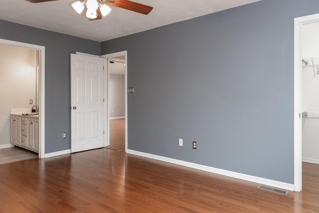 unfurnished bedroom featuring ensuite bathroom, wood finished floors, visible vents, baseboards, and a spacious closet