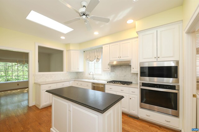kitchen featuring appliances with stainless steel finishes, ceiling fan, light wood-style flooring, white cabinetry, and tasteful backsplash