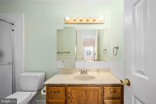 full bathroom featuring vanity, toilet, a shower with door, and wainscoting