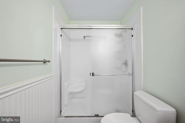 bathroom with wainscoting, toilet, and a shower stall