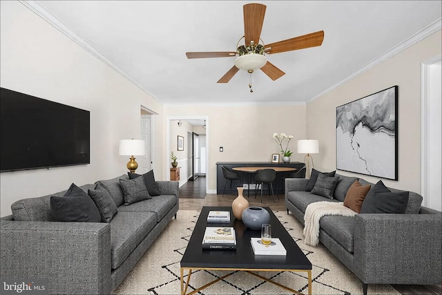 living area with baseboards, a ceiling fan, wood finished floors, and crown molding