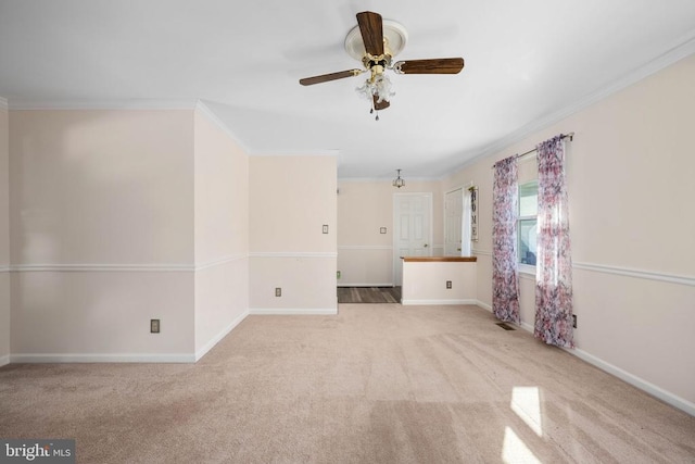 carpeted spare room with baseboards, ceiling fan, and crown molding