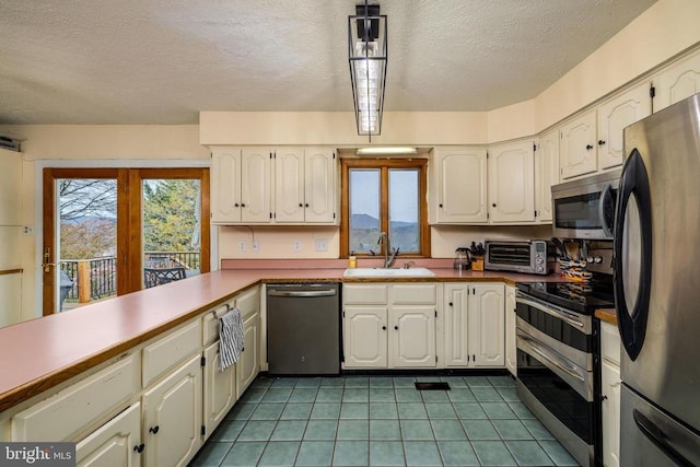 kitchen with stainless steel appliances, a sink, a textured ceiling, light tile patterned floors, and a peninsula