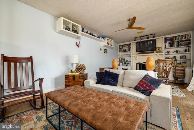 living area featuring hardwood / wood-style floors, ceiling fan, a textured ceiling, and a fireplace