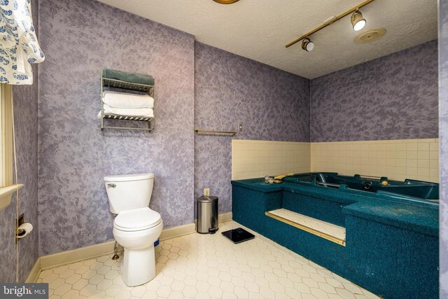 full bathroom with toilet, track lighting, tile patterned flooring, a textured ceiling, and a bathtub