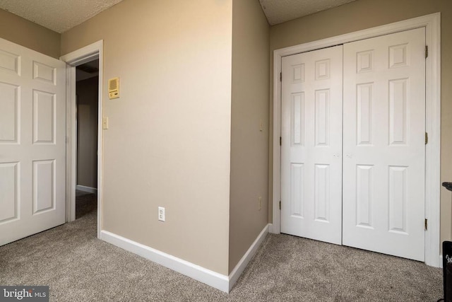 unfurnished bedroom featuring carpet, a closet, a textured ceiling, and baseboards